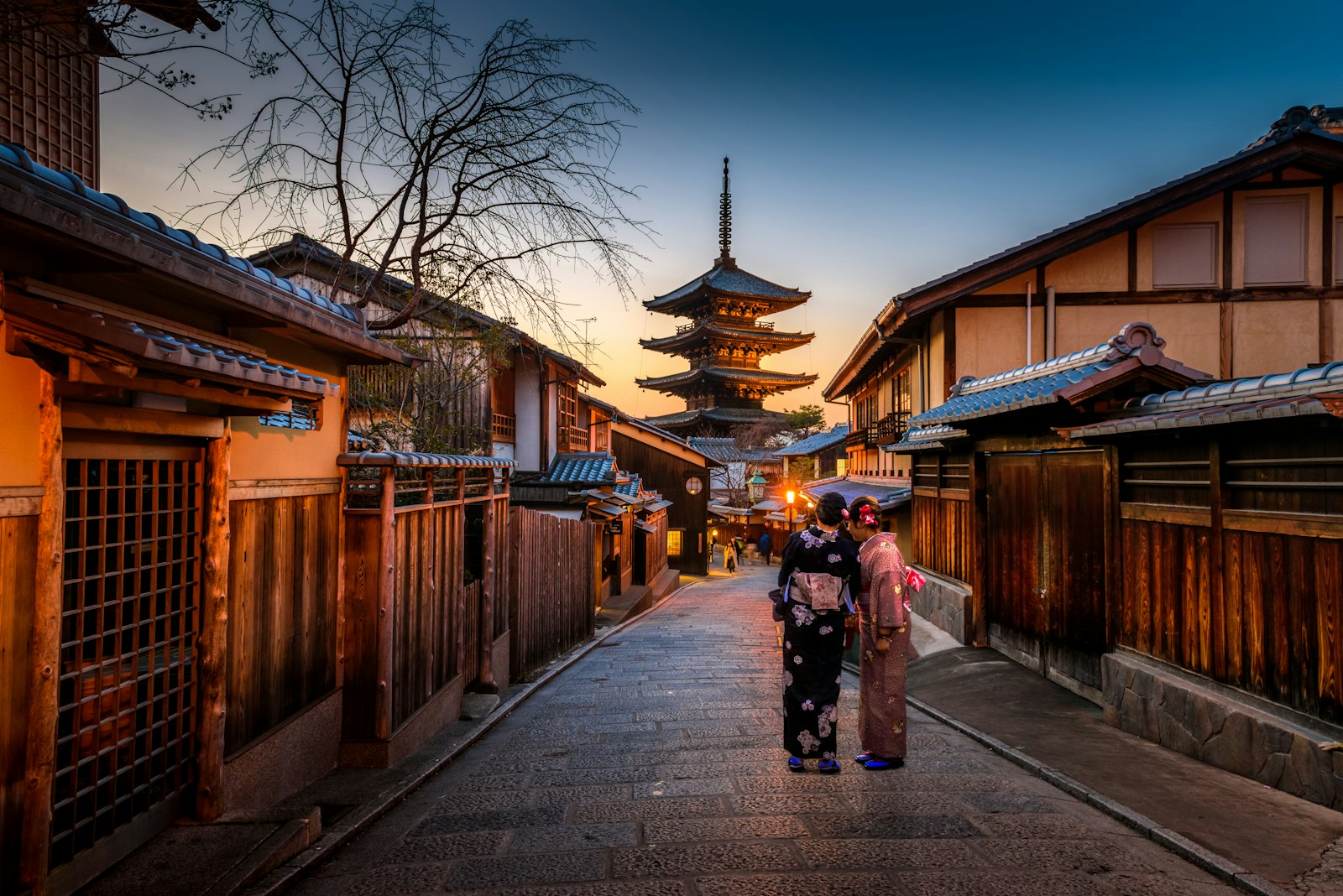 Two people in kimono walking a Kyoto street at dusk